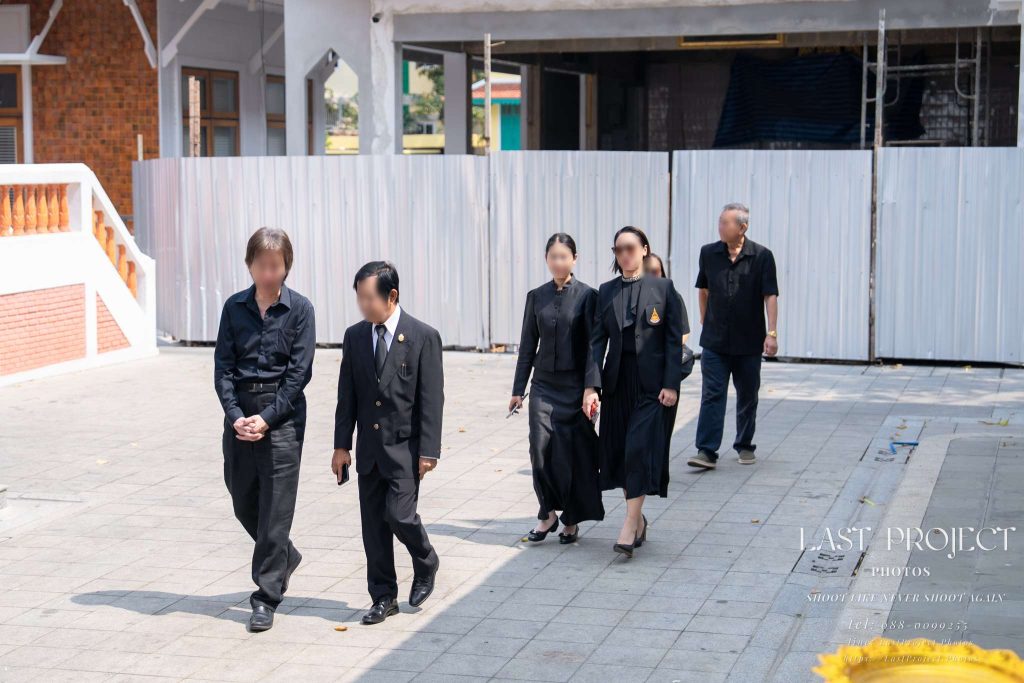 ภาพแขกแต่งกายชุดดำไว้ทุกข์ร่วมขบวนแห่เวียนรอบเมรุในพิธีฌาปนกิจ ณ วัดไทย Guests in black mourning attire walking in the funeral procession around the crematorium during a Thai Buddhist cremation ceremony at a temple