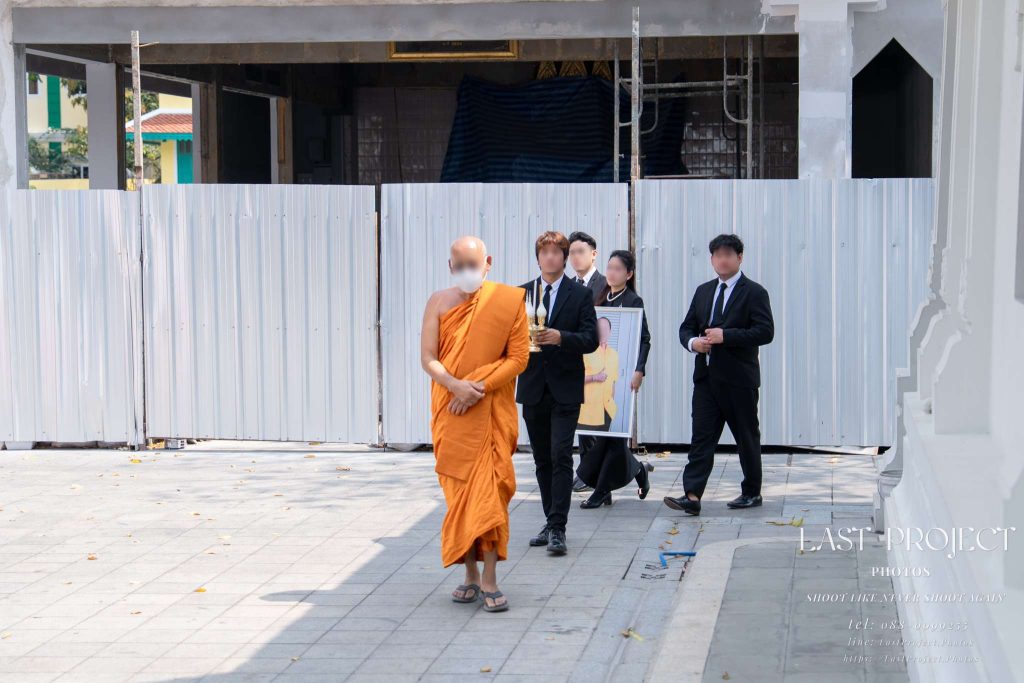 พระสงฆ์เดินนำขบวนเจ้าภาพถือกระถางธูปและรูปถ่ายผู้วายชนม์ในพิธีเวียนรอบเมรุงานฌาปนกิจศพแบบไทย Buddhist monk leading the host family holding incense and a deceased portrait during the circumambulation ritual at a Thai Buddhist funeral cremation ceremony
