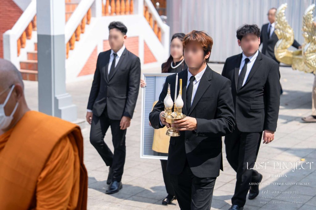 ภาพญาติผู้เสียชีวิตเดินเวียนรอบเมรุในพิธีฌาปนกิจศพ ณ วัดไทย Family members carrying ceremonial items during the circumambulation procession at a Thai Buddhist funeral crematorium ceremony