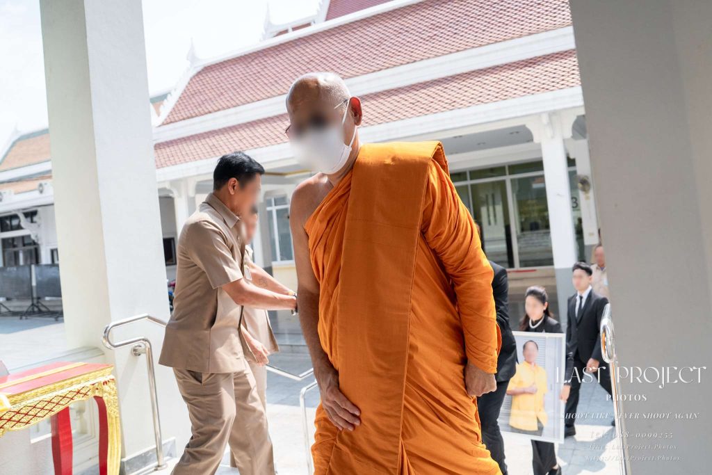พระสงฆ์สวมหน้ากากอนามัยและแว่นตากันแดดเดินนำขบวนงานฌาปนกิจศพขึ้นสู่เมรุ ณ วัดไทย A Buddhist monk wearing a face mask and sunglasses leading a Thai Buddhist funeral cremation procession up to the crematorium.