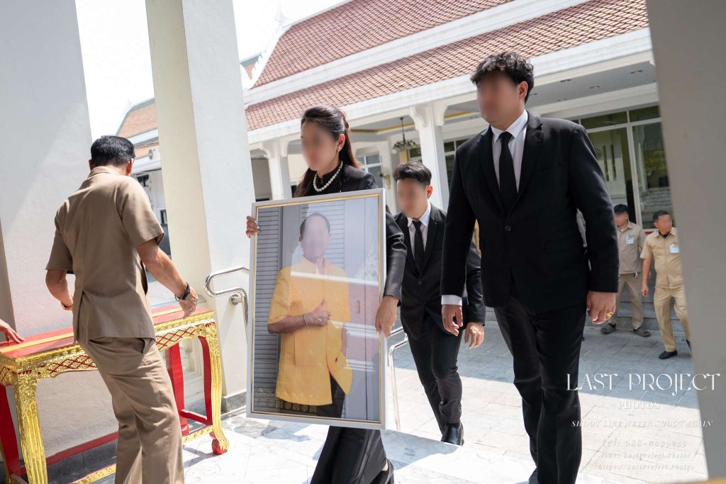 เจ้าภาพถือกรอบรูปผู้วายชนม์เดินขึ้นบันไดเมรุในพิธีฌาปนกิจศพแบบไทย Family members holding the portrait of the deceased ascending the crematorium stairs during a Thai Buddhist cremation ceremony