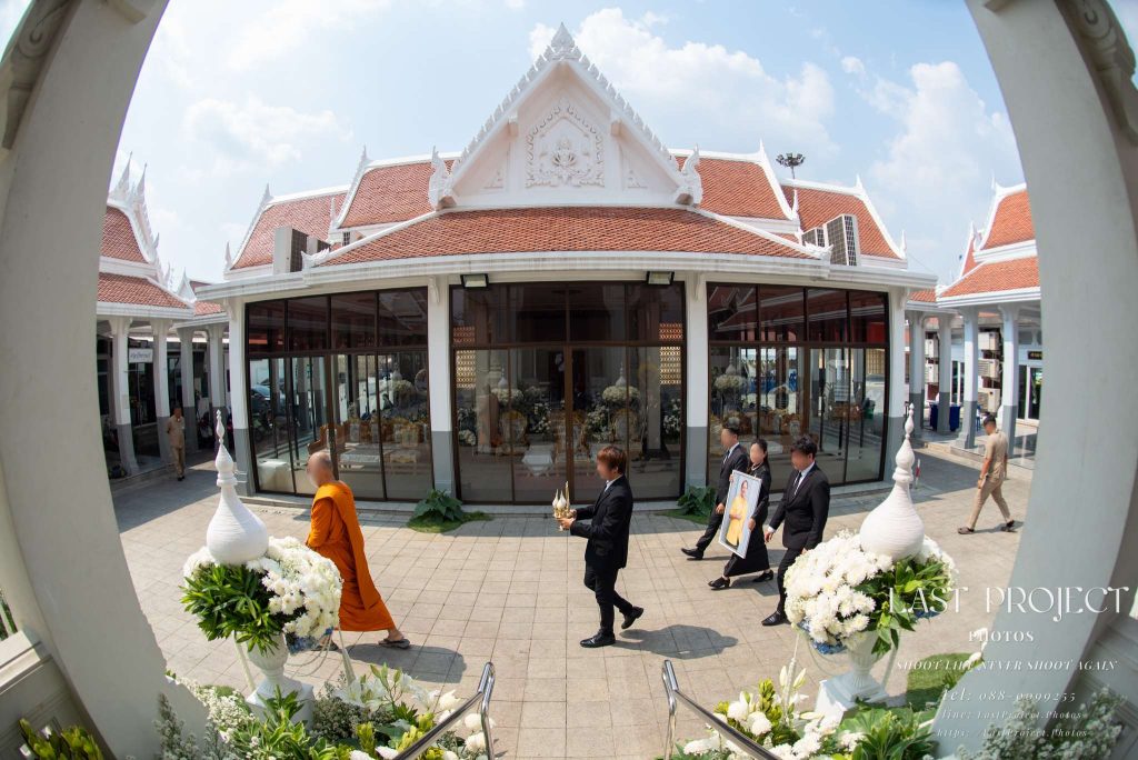 ช่างภาพถ่ายภาพมุมกว้างพิธีแห่เวียนรอบเมรุในงานศพไทย พระสงฆ์และญาติเดินนำหน้ารูปผู้วายชนม์ Funeral photographer capturing a wide-angle view of a traditional Thai Buddhist cremation procession around the meru crematorium