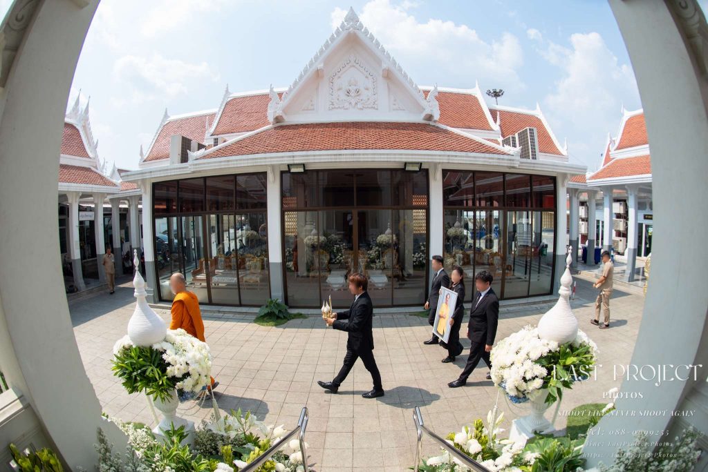 พิธีเวียนเมรุในงานฌาปนกิจ ณ วัดไทย นำขบวนโดยพระสงฆ์และญาติผู้ถือรูปผู้วายชนม์ Thai Buddhist funeral procession walking around the crematorium at a temple led by a monk and family holding the portrait of the deceased
