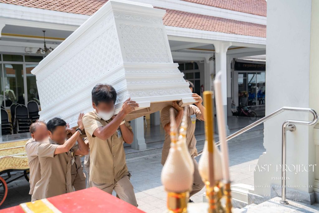 เจ้าหน้าที่กำลังแบกหีบศพสีขาวขึ้นเมรุในพิธีฌาปนกิจศพแบบไทย ณ วัดไทย Funeral staff carrying a white ornate casket up to the crematorium during a traditional Thai Buddhist cremation ceremony at a Thai temple
