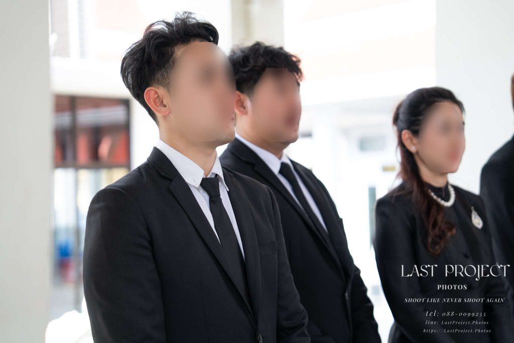ภาพถ่ายเจ้าภาพและครอบครัวในชุดไว้ทุกข์สีดำยืนร่วมพิธีฌาปนกิจบนเมรุวัดไทย Host family in black mourning suits standing with solemn expressions during a Thai Buddhist cremation ceremony at a temple crematorium