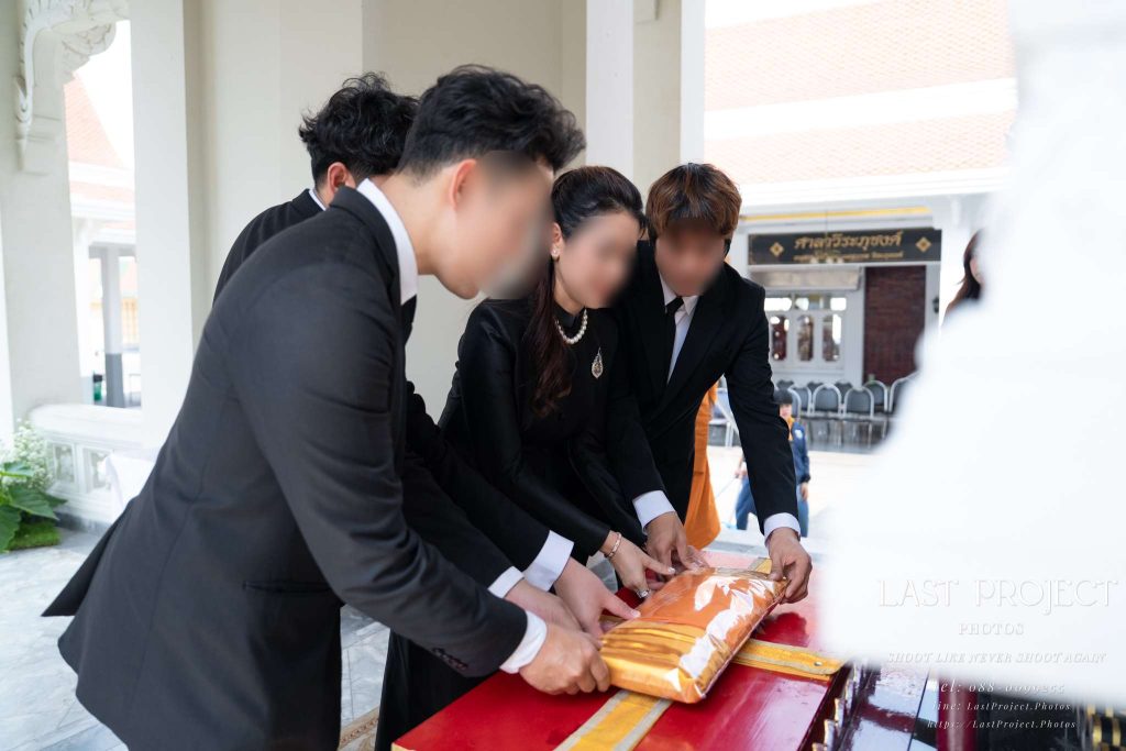 ภาพญาติกำลังทอดผ้าไตรหน้าหีบศพบนเมรุในพิธีฌาปนกิจศพวัดไทย Family offering monastic robes on the altar before the casket during a traditional Thai Buddhist funeral cremation ceremony at a temple
