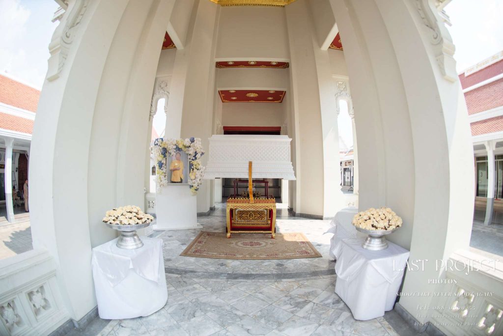 หีบศพสีขาวตั้งบนเมรุวัดไทยในพิธีฌาปนกิจศพพร้อมพานดอกไม้จันทน์ White coffin placed on a traditional Thai temple crematorium during a Buddhist funeral cremation ceremony