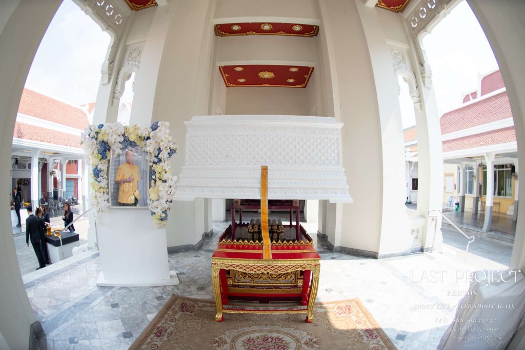 ภาพถ่ายมุมกว้างหีบศพสีขาวตั้งบนเมรุวัดไทยในพิธีฌาปนกิจ Wide-angle view of a white coffin positioned on the crematorium pavilion during a traditional Thai Buddhist funeral ceremony