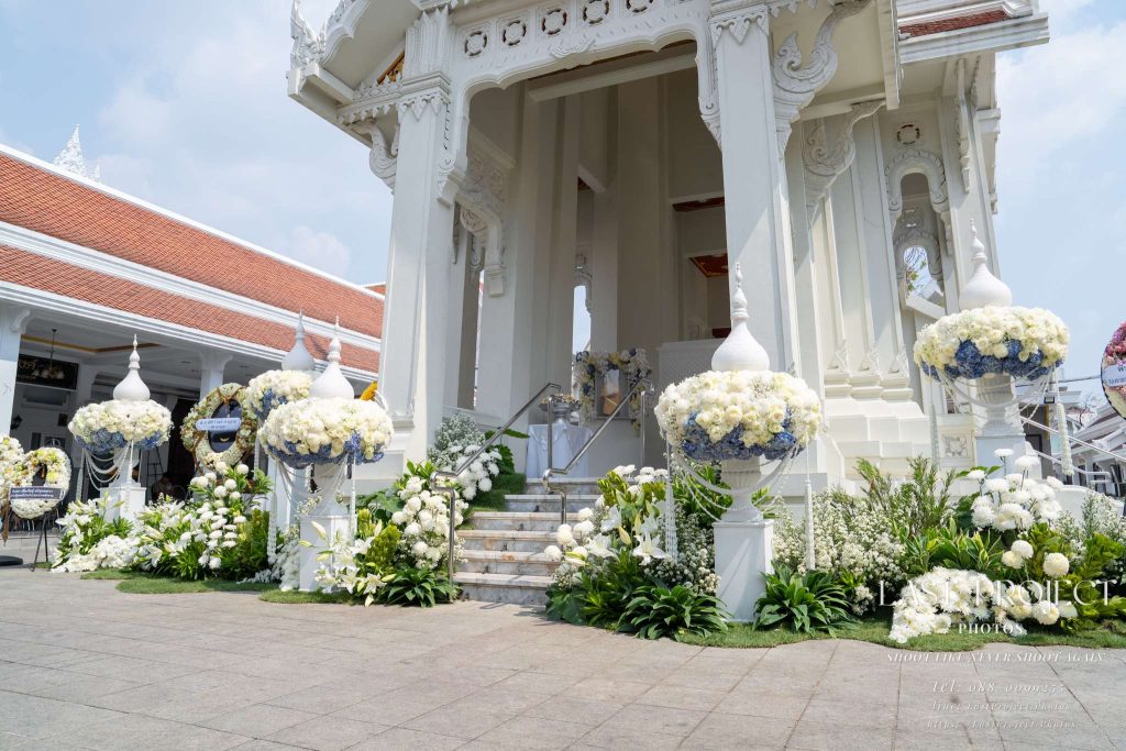 การตกแต่งดอกไม้สดโทนสีขาวและฟ้าบริเวณบันไดทางขึ้นเมรุในพิธีฌาปนกิจวัดไทย Elegant white and blue floral decorations adorning the crematorium staircase at a Thai temple cremation ceremony
