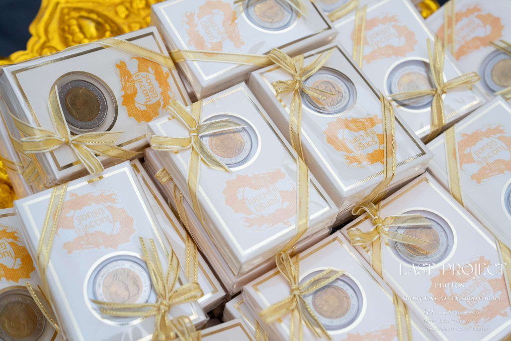 ของชำร่วยงานศพเหรียญที่ระลึก 10 บาทในกล่องผูกโบสีทอง ถ่ายด้วยเลนส์มาโครในงานฌาปนกิจ ณ วัดไทย Funeral favor commemorative coins in gold ribbon boxes captured with a macro lens at a Thai temple cremation ceremony