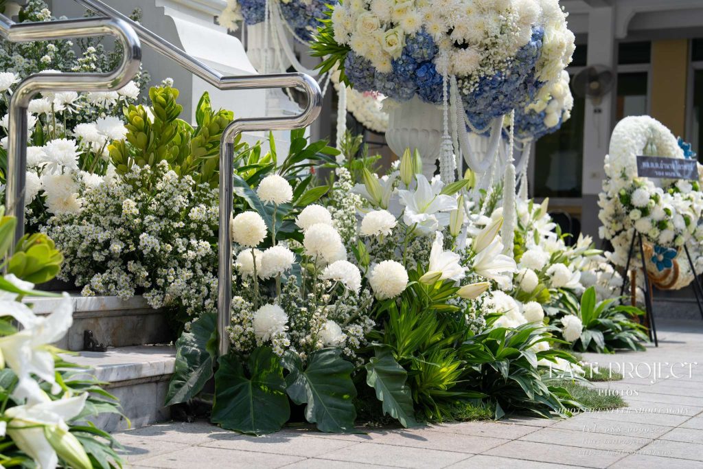 ซุ้มดอกไม้สดสีขาวประดับบันไดทางขึ้นเมรุในพิธีฌาปนกิจศพ ณ วัดไทย Elegant white floral arrangement decorating the crematorium staircase at a traditional Thai funeral ceremony in a Buddhist temple