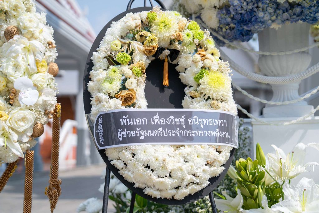 ภาพถ่ายเจาะรายละเอียดพวงหรีดดอกไม้สดแสดงความอาลัยในพิธีฌาปนกิจ ณ วัดไทย Close-up of a fresh flower condolence wreath at a Thai funeral cremation ceremony at a Thai Buddhist temple.