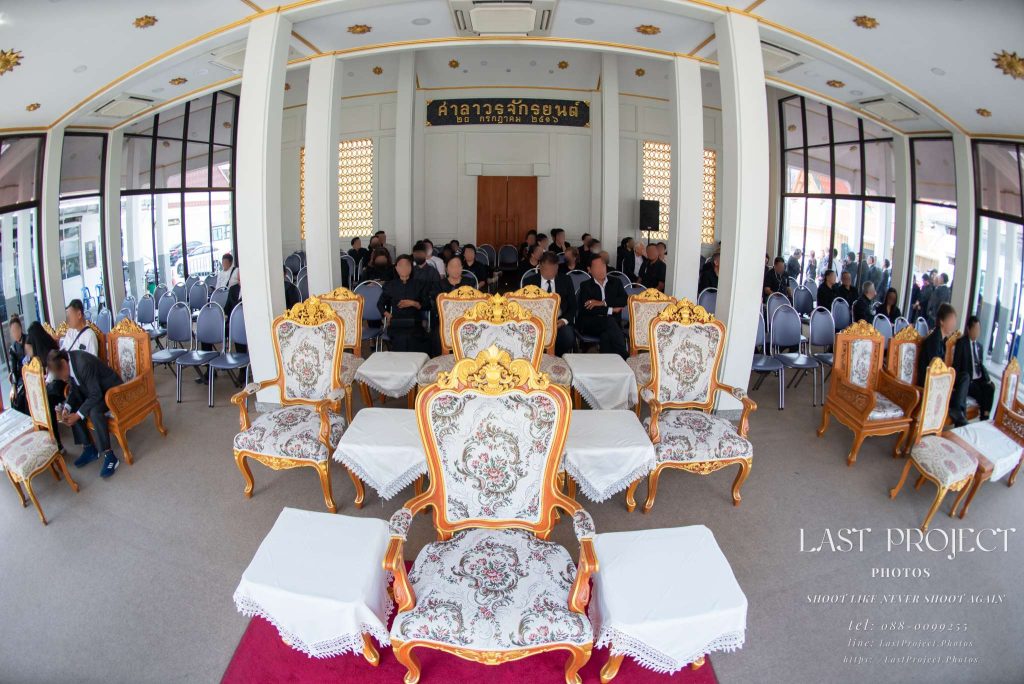 บรรยากาศภายในศาลาพิธีฌาปนกิจศพวัดไทย ถ่ายด้วยเลนส์มุมกว้างแสดงการจัดที่นั่งรับรองและแขกผู้ร่วมงาน Interior view of a Thai temple funeral pavilion with VIP ceremonial seating and attendees captured using a wide-angle lens