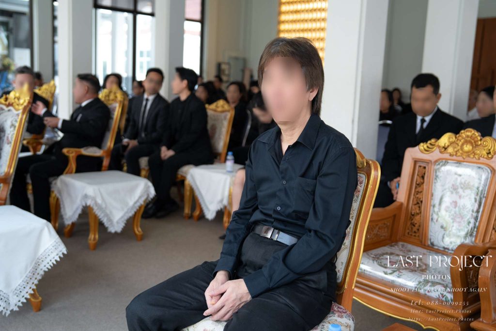 แขกผู้มีเกียรติสวมชุดไว้ทุกข์สีดำนั่งร่วมพิธีฌาปนกิจศพในวัดไทย Guests in black mourning attire seated during a traditional Thai Buddhist funeral and cremation ceremony