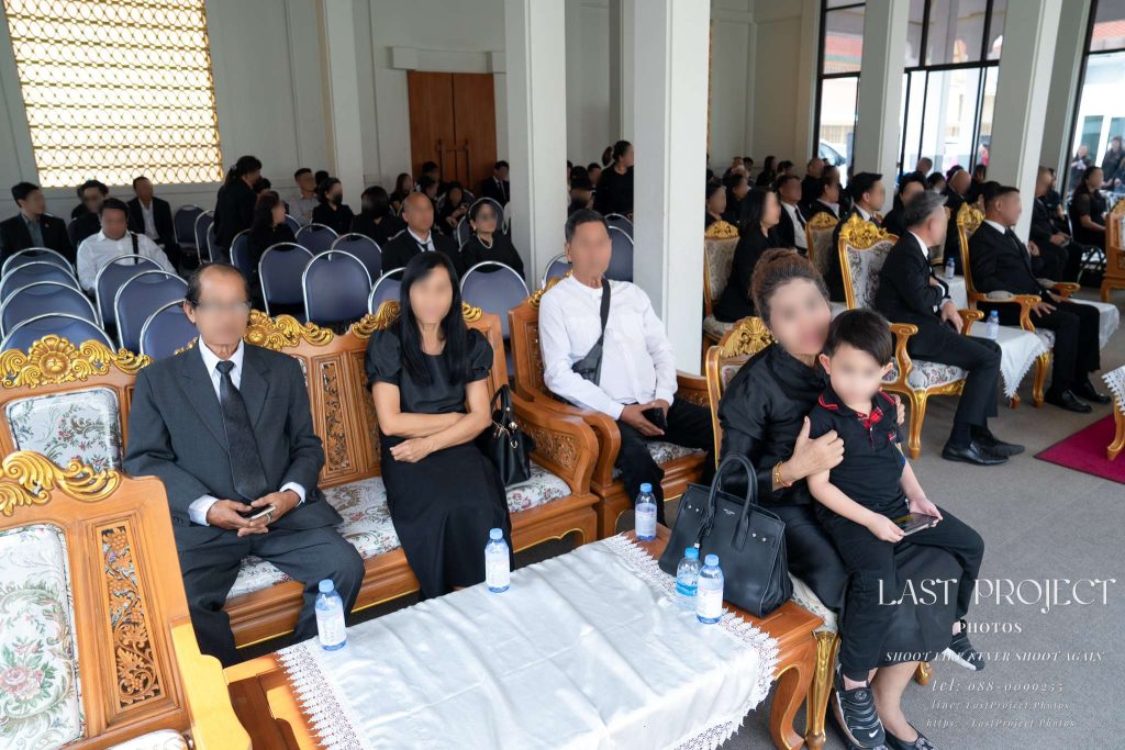 แขกและครอบครัวนั่งร่วมพิธีฌาปนกิจภายในศาลาวัด Guests and family members seated inside a Thai temple pavilion during a Buddhist funeral ceremony