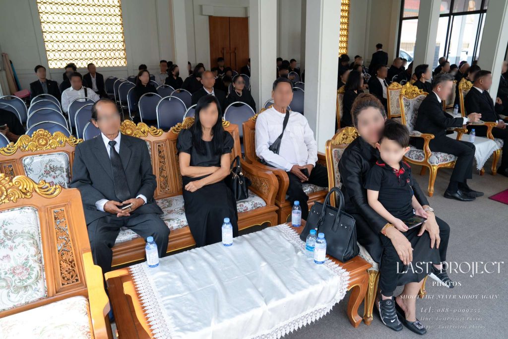 แขกและญาติสวมชุดไว้ทุกข์นั่งร่วมงานพิธีฌาปนกิจศพภายในศาลาวัดไทย Family and guests dressed in mourning attire seated together at a Buddhist funeral cremation ceremony inside a Thai temple pavilion