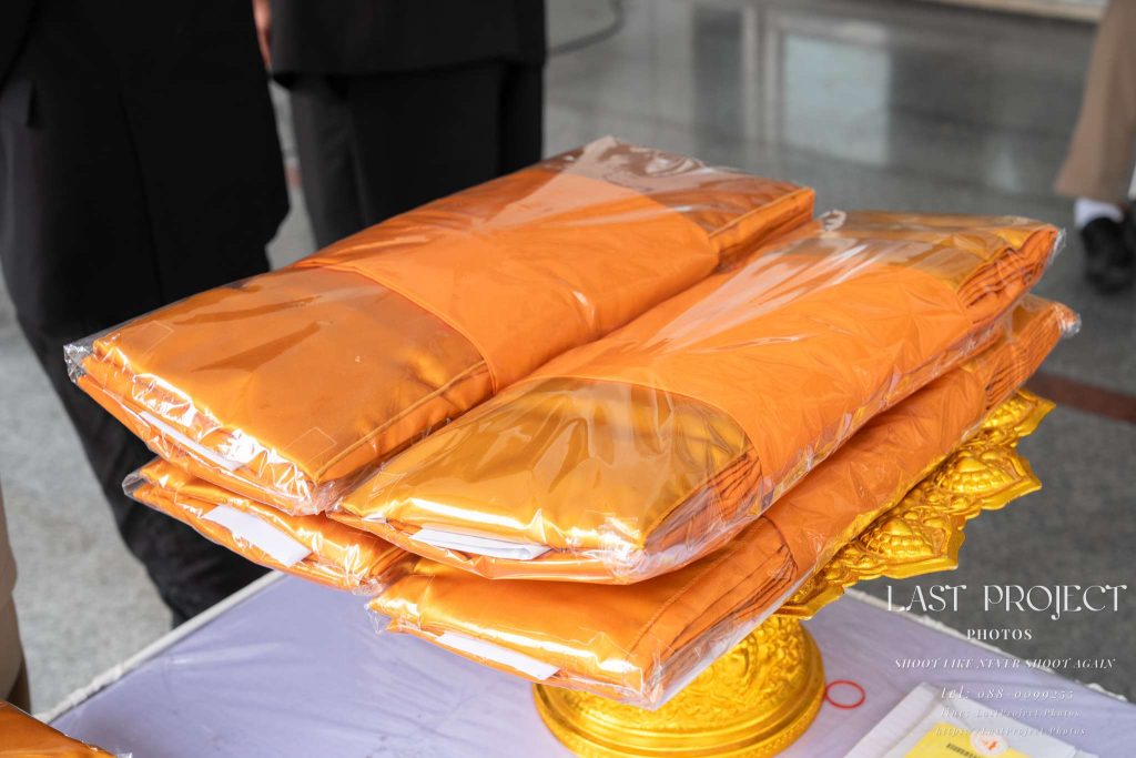ผ้าไตรบังสุกุลในห่อพลาสติกบนพานทองในศาลาวัดสำหรับพิธีฌาปนกิจ Saffron robes (Pha Trai Bangsukun) in plastic wrappers on a golden tray (Phan) inside a Thai temple pavilion for a cremation ceremony.
