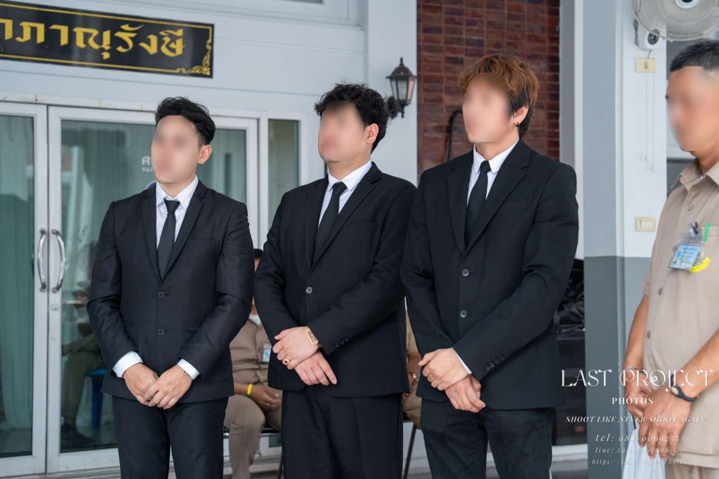 เจ้าภาพชายในชุดสูทสีดำยืนรอเริ่มพิธีฌาปนกิจศพ ณ วัดไทย Host family members in formal black suits standing respectfully before the Buddhist cremation ceremony at a Thai temple