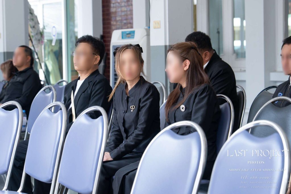 แขกผู้ร่วมงานสวมชุดดำนั่งรอพิธีฌาปนกิจศพ ณ ศาลาบำเพ็ญกุศลวัดไทย Guests in black mourning attire sitting in the funeral pavilion awaiting a Thai Buddhist cremation ceremony