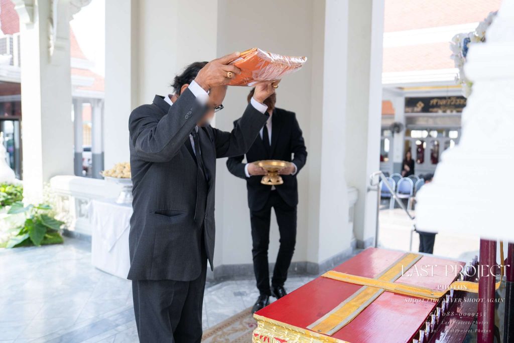 ภาพแขกผู้มีเกียรติยกผ้าไตรบังสุกุลขึ้นจบศีรษะในพิธีฌาปนกิจศพวัดไทย An honored guest raising funeral robes to pay respect during a Thai Buddhist cremation ceremony at a temple