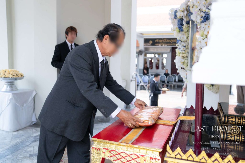 แขกผู้มีเกียรติกำลังวางผ้าไตรบังสุกุลหน้าหีบศพในพิธีฌาปนกิจ ณ เมรุวัดไทย Honored guest placing monastic robes before the casket during the Bangsukon ritual at a Thai Buddhist cremation ceremony.