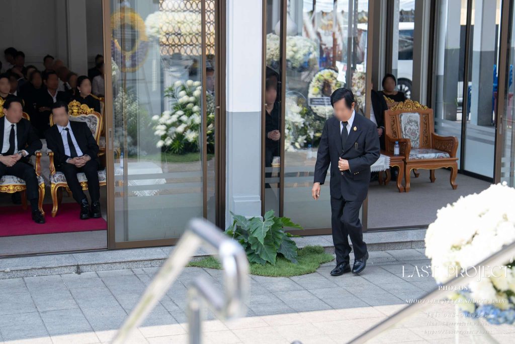 แขกผู้มีเกียรติกำลังเดินจากศาลาขึ้นเมรุในพิธีทอดผ้าไตรบังสุกุล งานพระราชทานเพลิงศพและงานฌาปนกิจ ณ วัดไทย Distinguished guest walking to the crematorium for the robe offering ritual during a Thai Buddhist funeral cremation ceremony