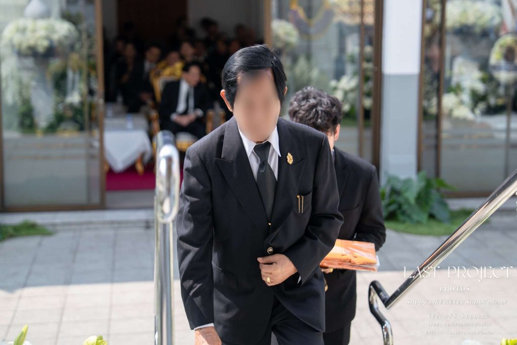 แขกผู้มีเกียรติสวมชุดสูทดำกำลังเดินขึ้นบันไดเมรุในพิธีฌาปนกิจศพ ณ วัดไทย A guest in a formal black suit walking up the stairs to the crematorium at a Thai Buddhist funeral ceremony