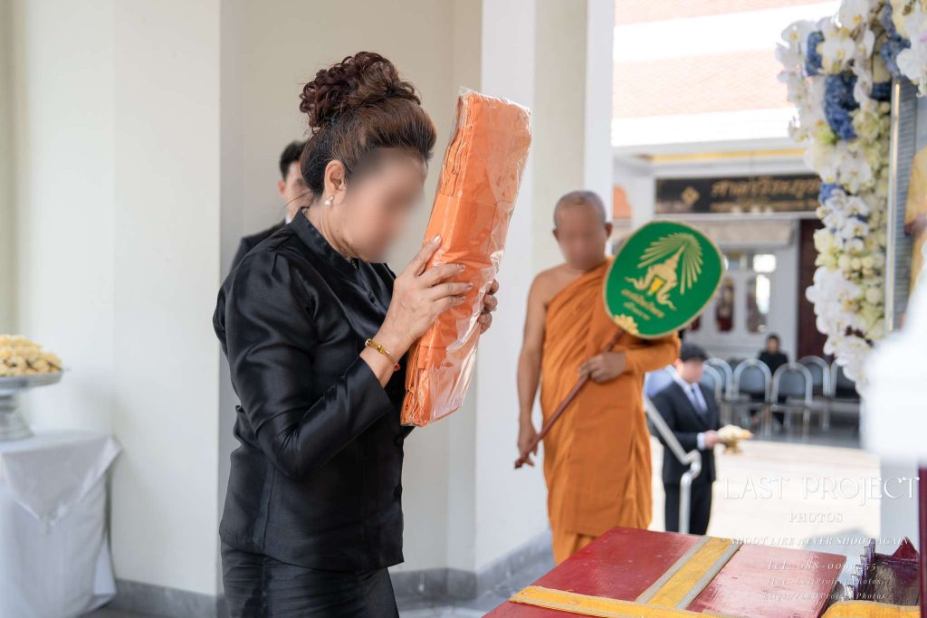 แขกสวมชุดดำยกผ้าไตรบังสุกุลจบศีรษะแสดงความเคารพในพิธีฌาปนกิจศพวัดไทย Guest in mourning black dress raising monk robes in prayer during a Thai Buddhist cremation ceremony