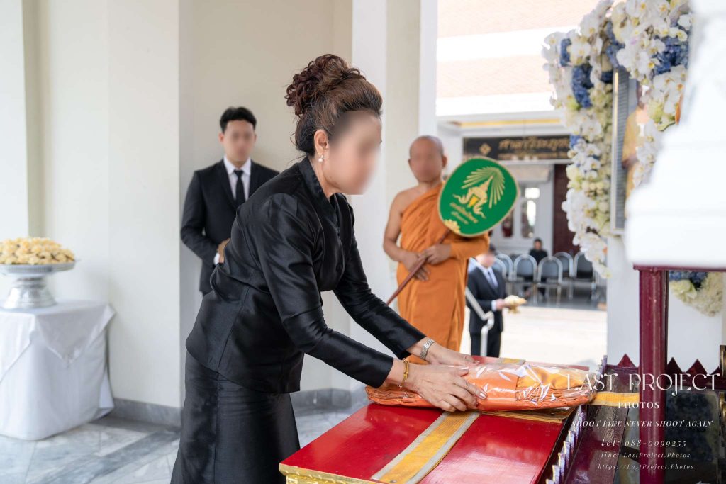 แขกผู้มีเกียรติขึ้นทอดผ้าไตรบังสุกุลหน้าหีบศพในพิธีฌาปนกิจศพ ณ เมรุวัดไทย An honorable guest offering saffron robes before the casket during a Thai Buddhist cremation ceremony at a temple