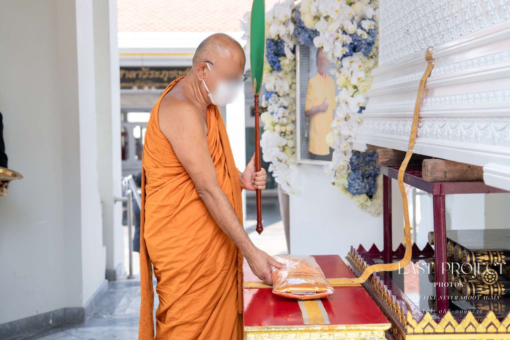 พระสงฆ์พิจารณาผ้าบังสุกุลหน้าหีบศพในพิธีฌาปนกิจ ณ เมรุวัดไทย Buddhist monk reciting prayers and considering Bangsukula robes in front of the casket during a Thai cremation ceremony at a temple