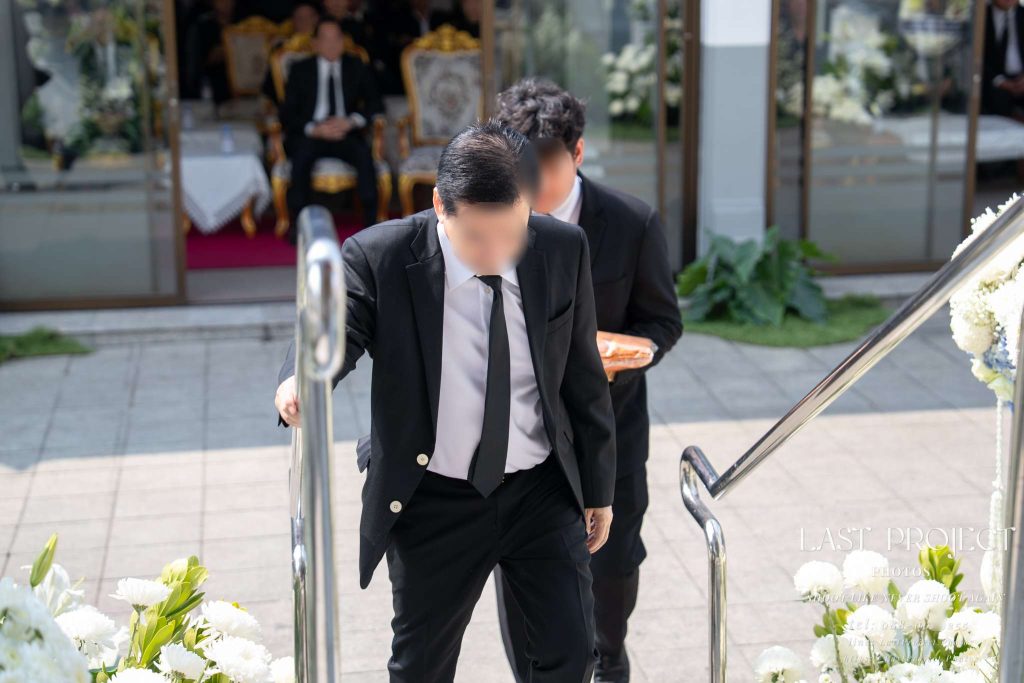 ภาพมุมสูงขณะแขกผู้มาร่วมงานในชุดดำกำลังเดินขึ้นบันไดเมรุเพื่อร่วมพิธีฌาปนกิจศพในวัดไทย Candid shot of guests in black attire walking up the stairs of a crematorium during a Thai Buddhist cremation ceremony at a temple