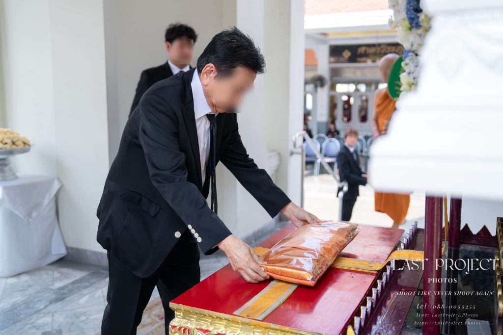 ภาพแขกผู้มีเกียรติทอดผ้าไตรบังสุกุลบนจิตกาธานในพิธีฌาปนกิจศพ An honorable guest placing Buddhist robes on the funeral pyre during a Thai Buddhist cremation ceremony.
