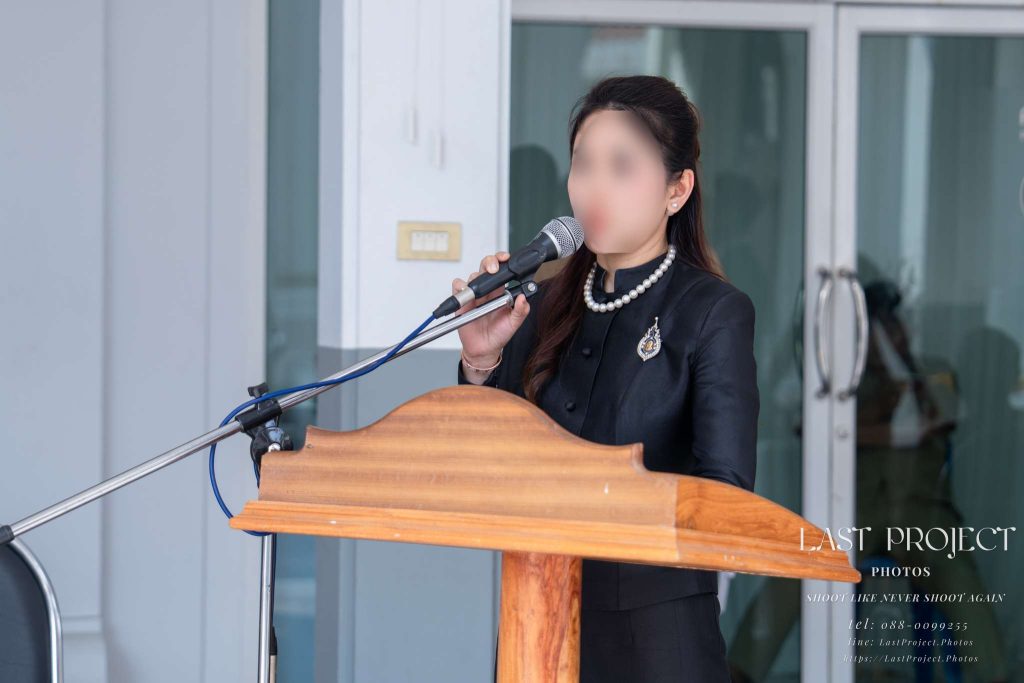 พิธีอ่านประวัติและกล่าวไว้อาลัยผู้วายชนม์ในพิธีฌาปนกิจ A woman giving a eulogy speech at the podium during a Buddhist funeral ceremony