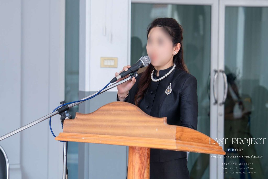 พิธีกรหญิงกล่าวคำไว้อาลัยและอ่านประวัติผู้วายชนม์บนโพเดียมในพิธีฌาปนกิจ Woman master of ceremonies reading the eulogy and biography of the deceased at the podium during a Thai Buddhist funeral cremation ceremony