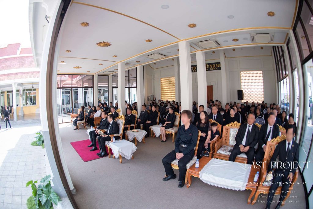 บรรยากาศแขกผู้ร่วมงานนั่งฟังสรุปประวัติผู้วายชนม์ภายในศาลาพิธีฌาปนกิจ Guests and relatives seated inside the temple pavilion during a Buddhist funeral ceremony