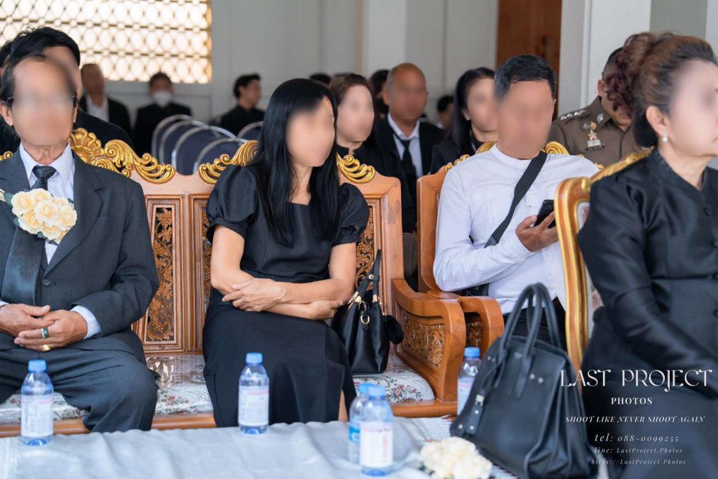 แขกผู้มีเกียรติสวมชุดไว้ทุกข์นั่งฟังการอ่านประวัติผู้วายชนม์ในพิธีฌาปนกิจศพ Guests dressed in black mourning attire seated and listening to the eulogy during a Thai cremation ceremony
