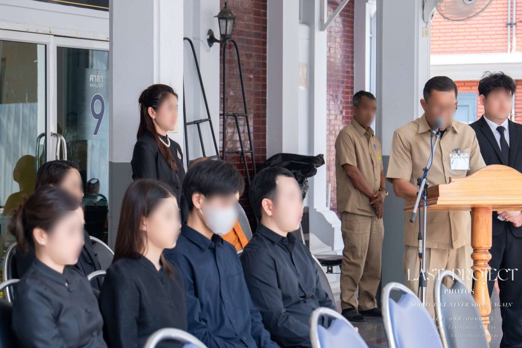 บรรยากาศพิธีฌาปนกิจศพ ณ วัดไทย เจ้าภาพและครอบครัวร่วมฟังพิธีกรกล่าวดำเนินพิธีการ Thai Buddhist cremation ceremony at a temple with the host and family listening to the master of ceremonies