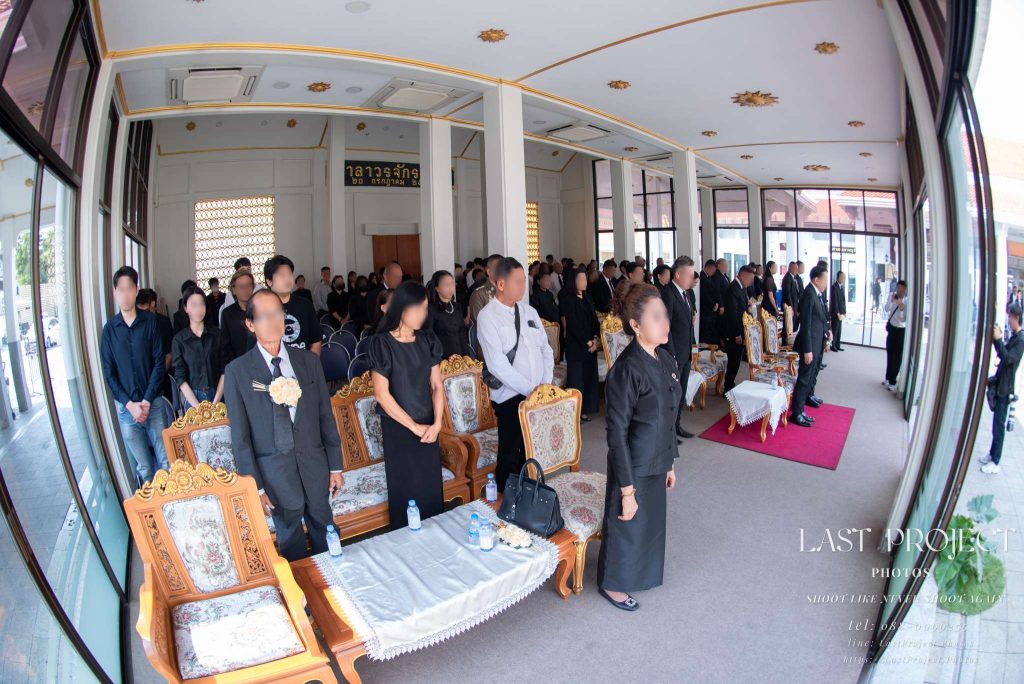 แขกผู้มีเกียรติยืนไว้อาลัยในศาลาพิธีฌาปนกิจศพ ภาพมุมกว้างด้วยเลนส์ฟิชอาย Guests standing in solemn remembrance inside a temple pavilion during a Thai cremation ceremony, captured with an ultra-wide fisheye lens.