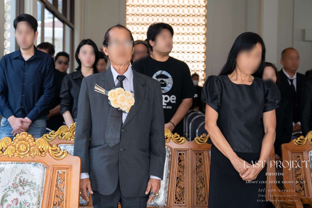 แขกคนสำคัญและญาติสนิทยืนสงบนิ่งไว้อาลัยในพิธีฌาปนกิจศพ ณ เมรุวัดไทย VIP guests and close relatives standing in silence at a Thai Buddhist cremation ceremony.