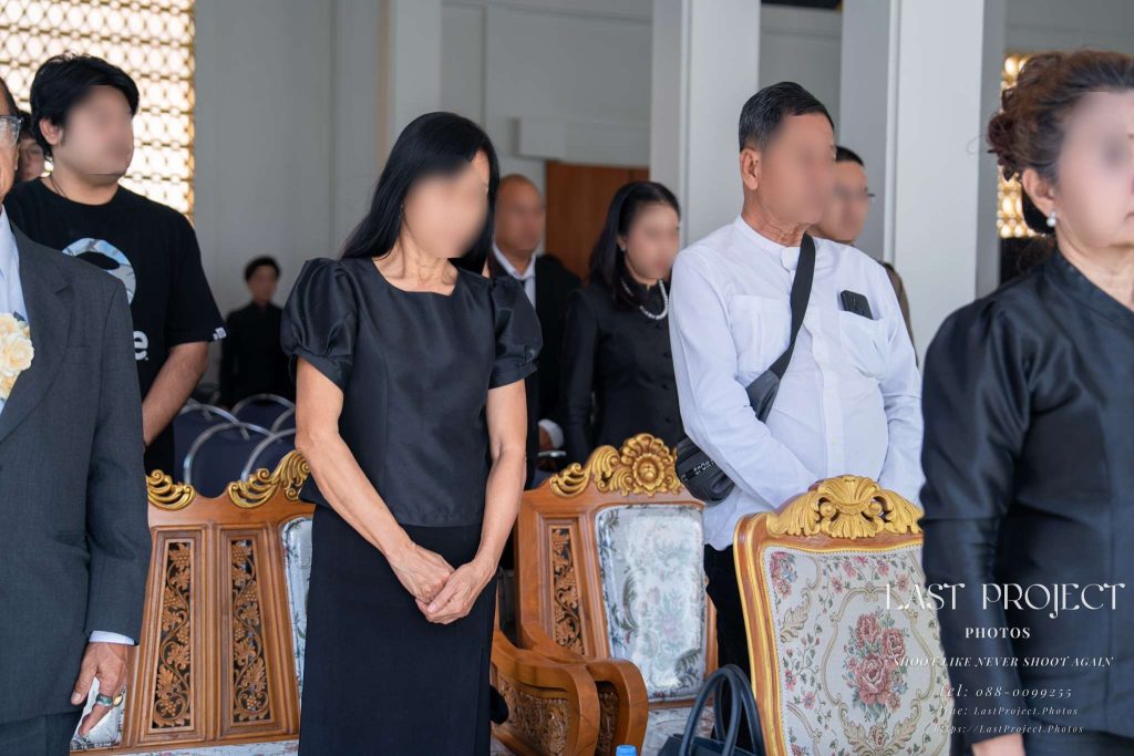 แขกผู้มีเกียรติยืนสงบนิ่งร่วมไว้อาลัยแก่ผู้วายชนม์ในพิธีฌาปนกิจศพ ณ วัดไทย Guests standing in silence to pay tribute to the deceased during a Buddhist cremation ceremony at a Thai temple