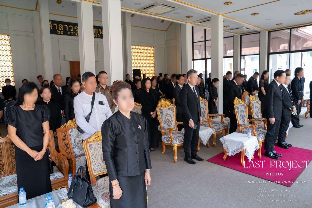 แขกและญาติร่วมยืนไว้อาลัยในชุดไว้ทุกข์สีดำในพิธีฌาปนกิจศพ ณ ศาลาวัด Guests and family members standing in black mourning attire to pay final respects at a Thai Buddhist cremation ceremony in a temple pavilion