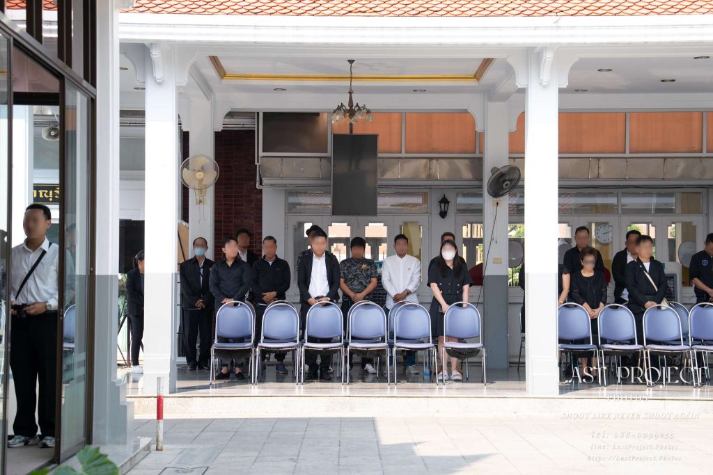 แขกผู้มีเกียรติร่วมยืนสงบนิ่งไว้อาลัยในพิธีฌาปนกิจศพ ณ ศาลาวัดเทพศิรินทร์ Guests standing in silence at the adjacent pavilion during a Buddhist cremation ceremony at Wat Thepsirin