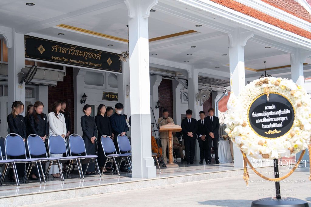 เจ้าภาพและแขกผู้มีเกียรติยืนสงบนิ่งไว้อาลัยแด่ผู้วายชนม์ในพิธีฌาปนกิจศพ ณ วัดไทย Hosts and guests standing in silence to pay tribute to the deceased during a Thai Buddhist cremation ceremony at a temple