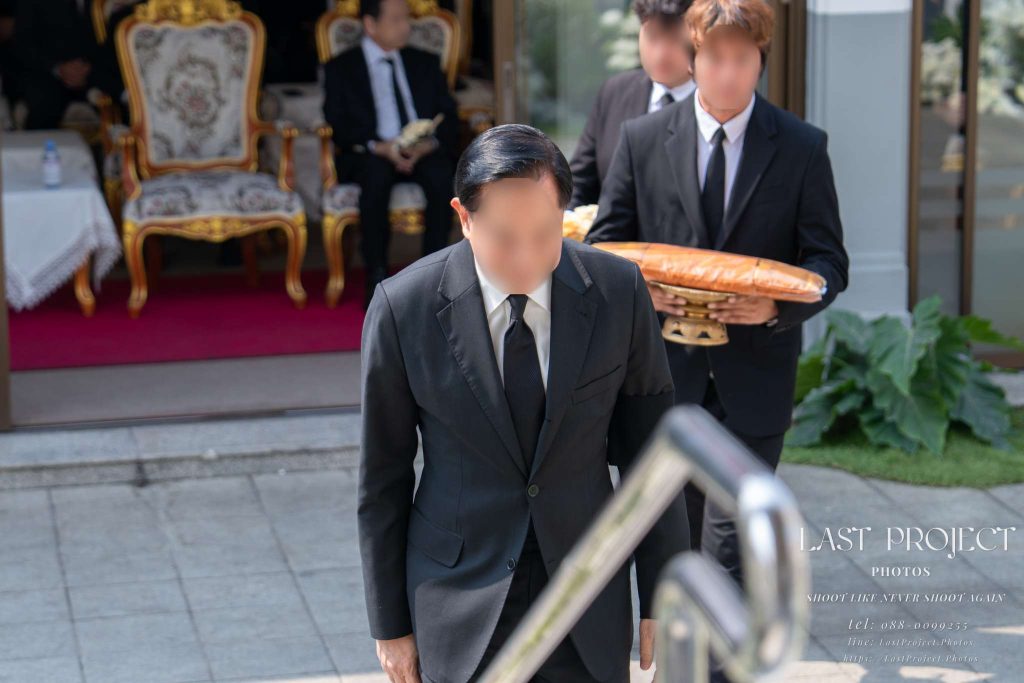 แขกผู้มีเกียรติแต่งกายชุดสูทดำกำลังเดินขึ้นบันไดเมรุในพิธีฌาปนกิจศพ A guest in a black suit walking up the crematorium stairs during a Thai Buddhist cremation ceremony