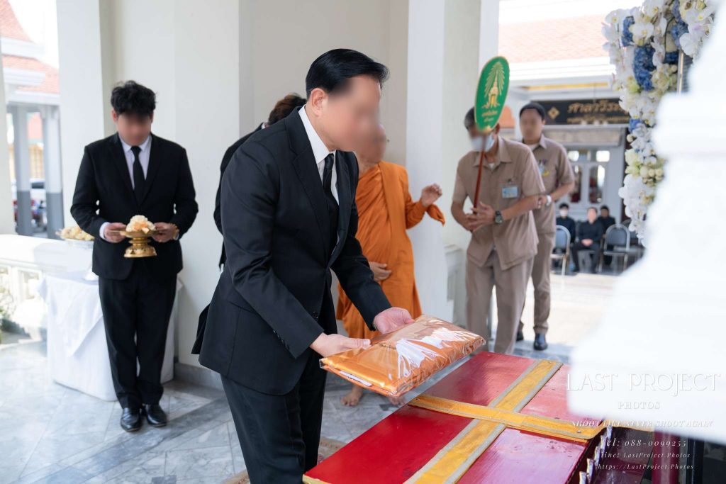 แขกผู้มีเกียรติวางผ้าไตรบังสุกุลหน้าหีบศพในพิธีฌาปนกิจศพ An honorable guest placing a Bangsukula monk robe on the pedestal before the casket during a Thai Buddhist cremation ceremony