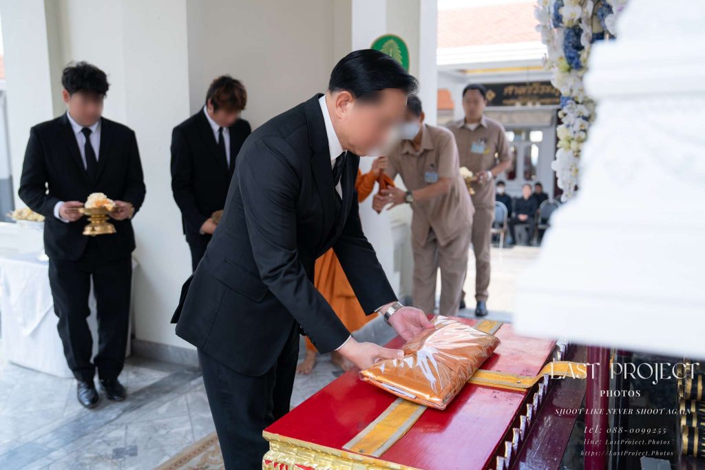 ภาพพิธีทอดผ้าไตรบังสุกุลหน้าหีบศพในพิธีฌาปนกิจศพ ณ เมรุวัดไทย A guest of honor offering a saffron Bangsukula robe before the casket during a Buddhist cremation ceremony at a Thai temple