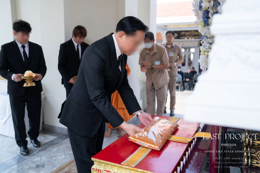 พิธีทอดผ้าไตรบังสุกุลหน้าหีบศพเพื่ออุทิศส่วนกุศลในงานฌาปนกิจศพตามประเพณีไทย Guest placing Buddhist robes before the casket during a traditional Thai funeral cremation ceremony.
