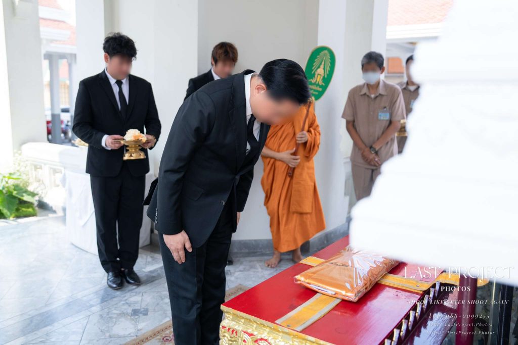แขกผู้มีเกียรติค้อมตัวเคารพศพหลังทอดผ้าไตรบังสุกุลหน้าหีบศพในพิธีฌาปนกิจศพวัดไทย A guest bowing to pay respects after offering robes before the casket during a Thai Buddhist cremation ceremony