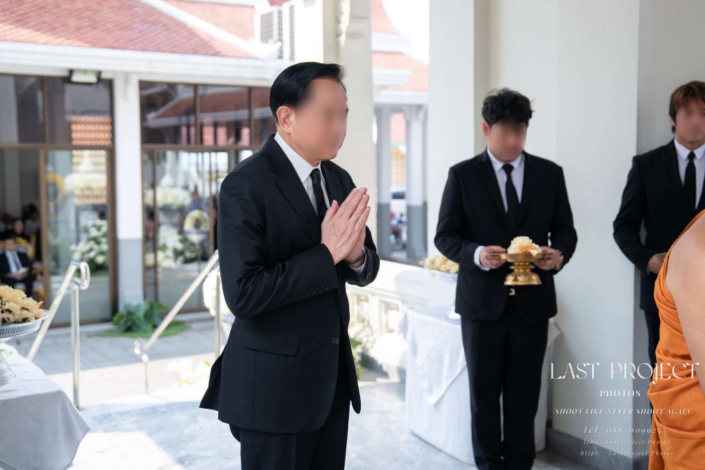 เจ้าภาพยืนพนมมือรอพระสงฆ์พิจารณาผ้าบังสุกุลในพิธีฌาปนกิจศพ Funeral host with hands folded in prayer awaiting the Buddhist monk during a cremation ceremony