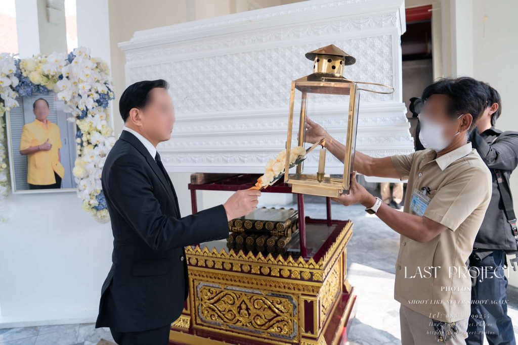 ประธานในพิธีจุดไฟดอกไม้จันทน์ในพิธีเผาหลอกหน้าหีบศพสีขาว ณ เมรุวัดไทย Presiding guest lighting a sandalwood flower for the symbolic cremation ceremony in front of a white casket at a Thai Buddhist temple